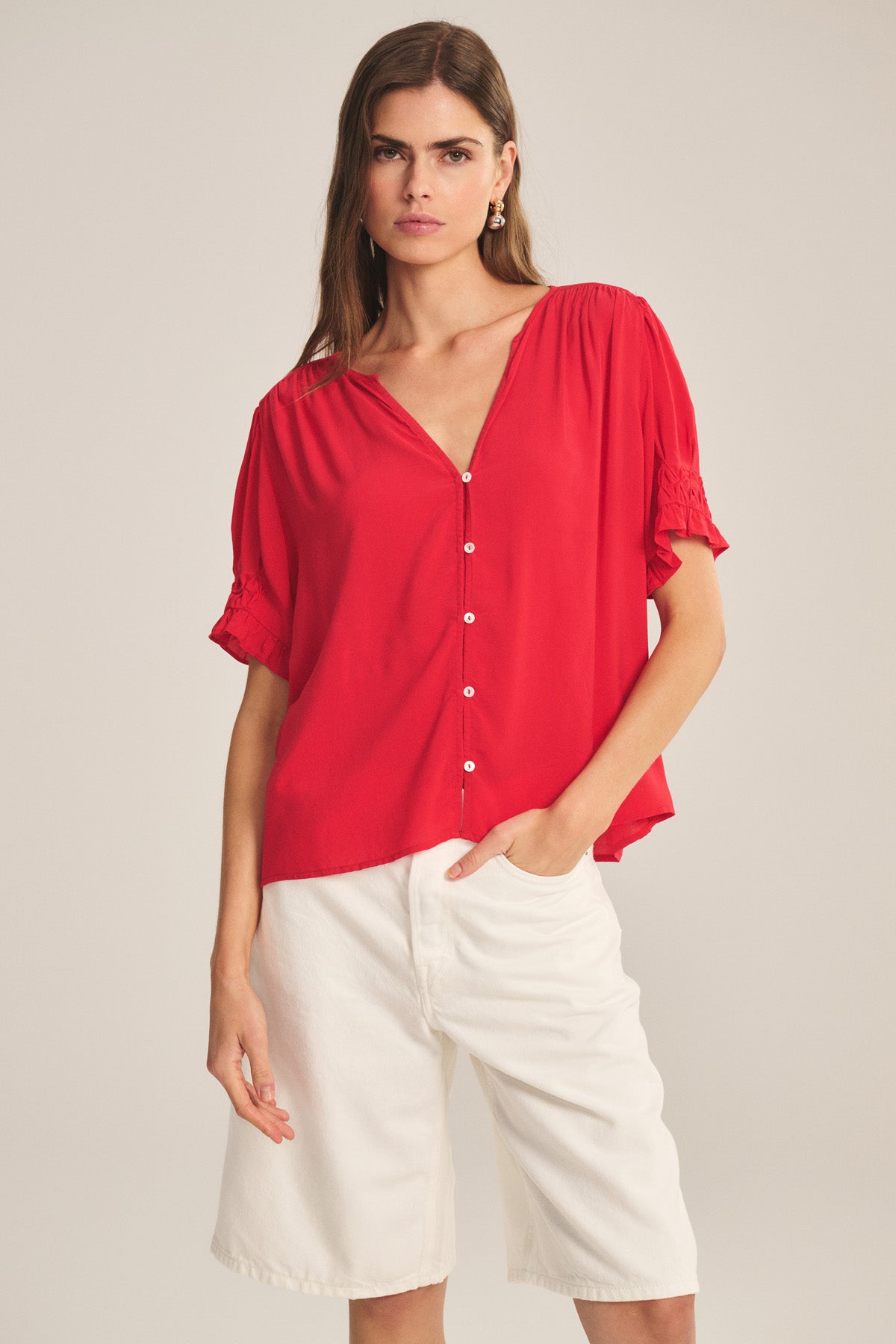 A woman models the CARMELLA TOP by Velvet by Graham & Spencer, a loose-fitting red rayon challis blouse with short sleeves, paired with white knee-length shorts against a plain background.