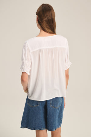 A person with long brown hair is shown from the back, wearing the Velvet by Graham & Spencer CARMELLA TOP and blue denim shorts against a plain background.