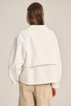 A person with long brown hair is shown from the back, wearing the CARRINGTON JACKET by Velvet by Graham & Spencer in white cotton twill, paired with beige pants against a plain background.