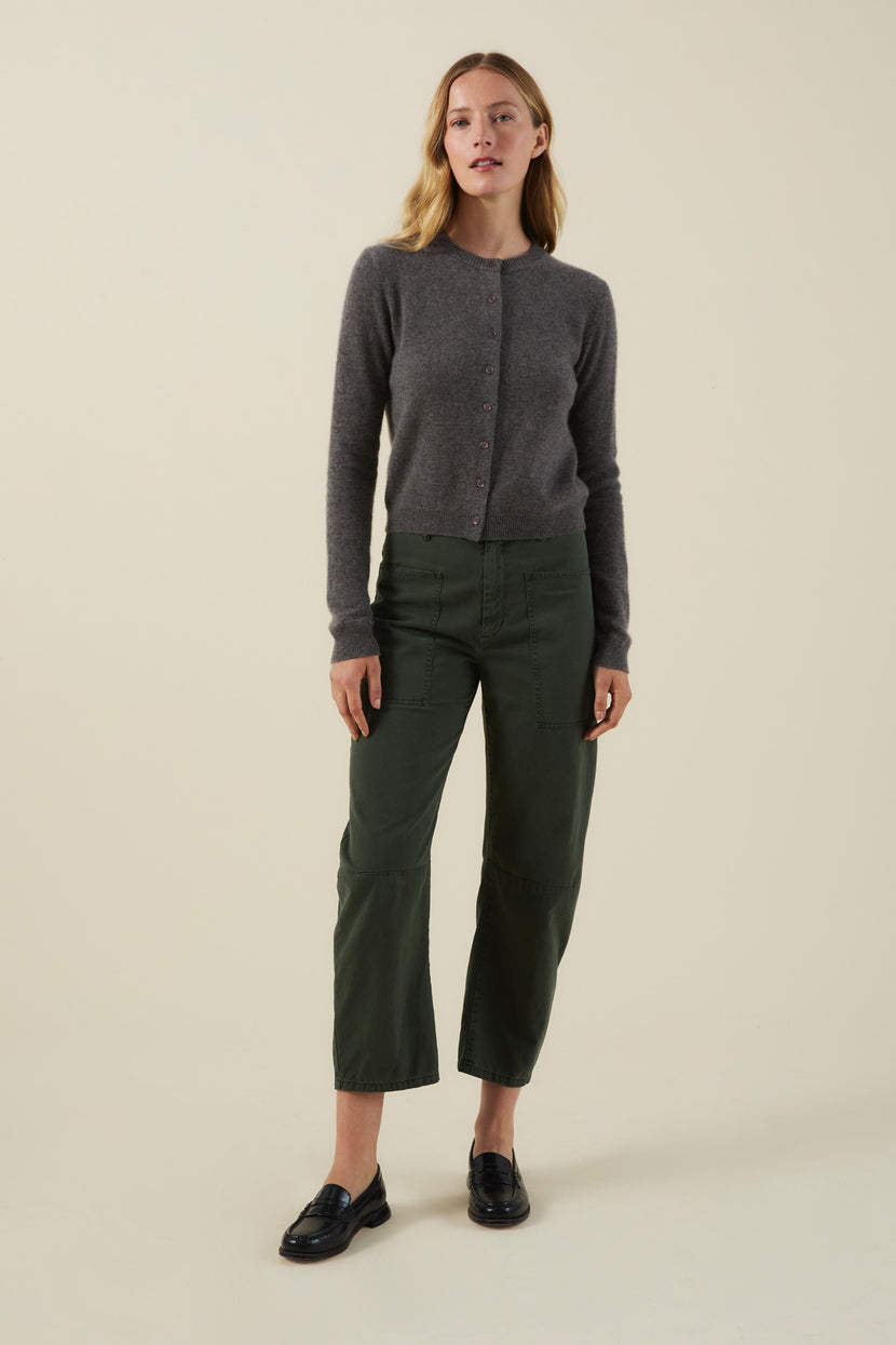 A person wearing a grey cropped AYLINA CASHMERE CARDIGAN, dark green utility pants, and black loafers.