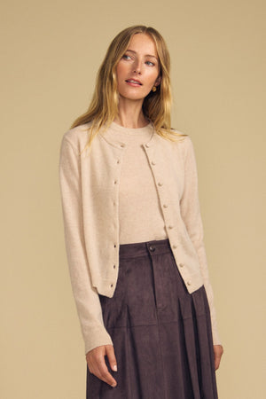 A woman wearing the AYLINA CASHMERE CARDIGAN by Velvet by Graham & Spencer, paired with a matching women’s layering sweater and a dark brown skirt, stands against a plain beige background.