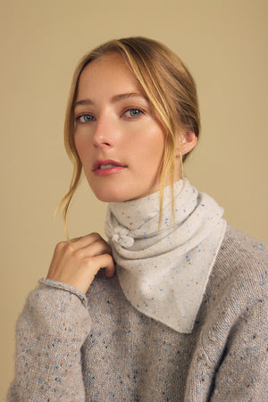 A woman with blonde hair wears the HELEN CASHMERE SCARF by Velvet by Graham & Spencer, styled with a matching neutral speckled sweater, looking at the camera against a beige background.