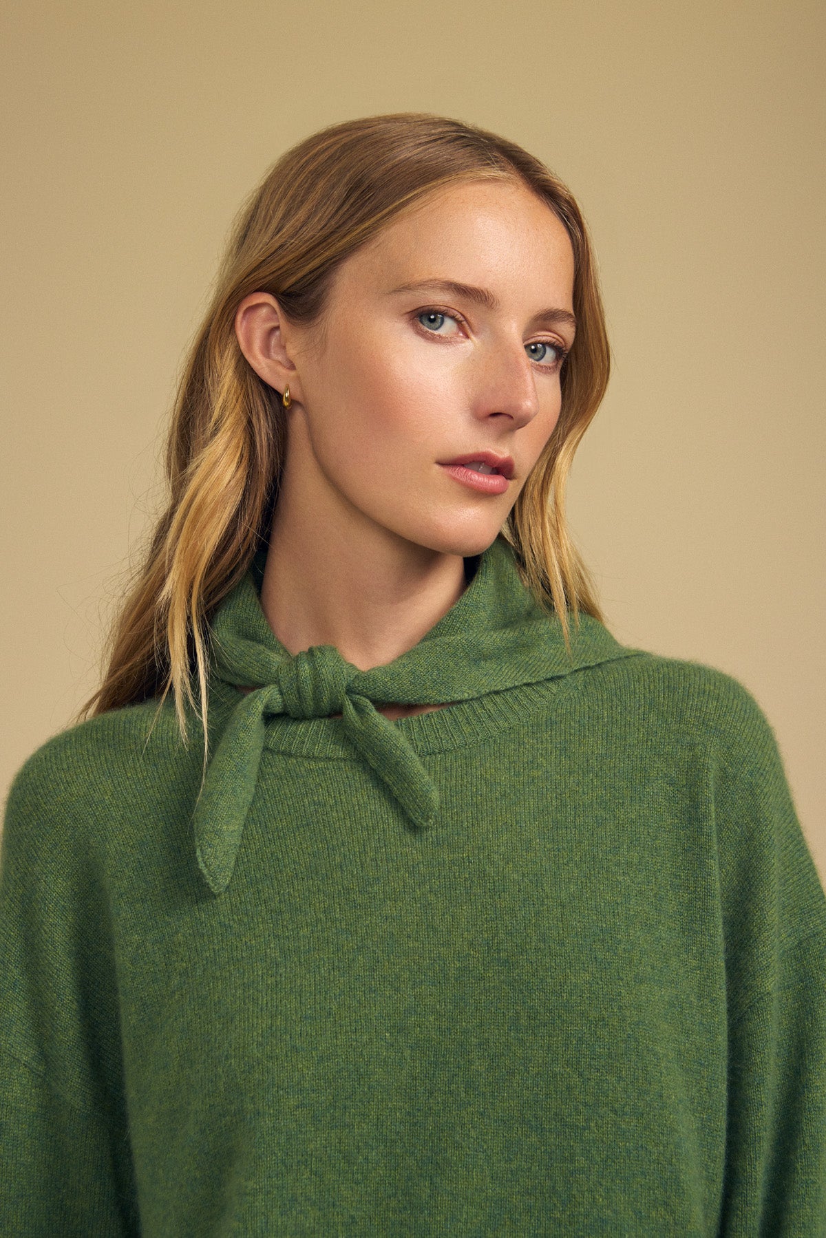 A woman with long blonde hair is wearing a green sweater with a tied collar and the HELEN CASHMERE SCARF by Velvet by Graham & Spencer, posing against a beige background.-41960847442113