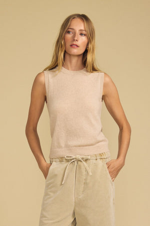 A woman stands against a beige background wearing the IVANA CASHMERE SWEATER VEST by Velvet by Graham & Spencer, paired with light tan drawstring pants and her hands in her pockets—the perfect look for effortless layering.