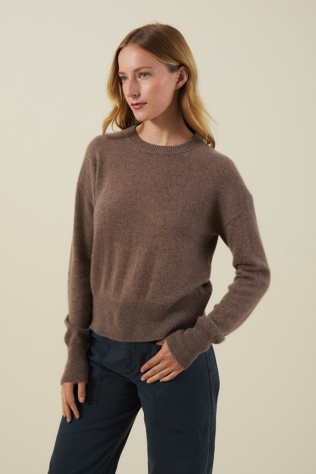 Woman wearing an ALBA CASHMERE SWEATER in soft knit brown with long sleeves and a crewneck, paired with dark trousers.-46498787229889