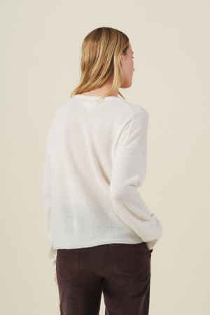 A person with long, light brown hair is shown from behind against a plain, light-colored background, wearing the AMIKA Cashmere Sweater by Velvet by Graham & Spencer—a white, cropped-waist design—paired with dark pants.