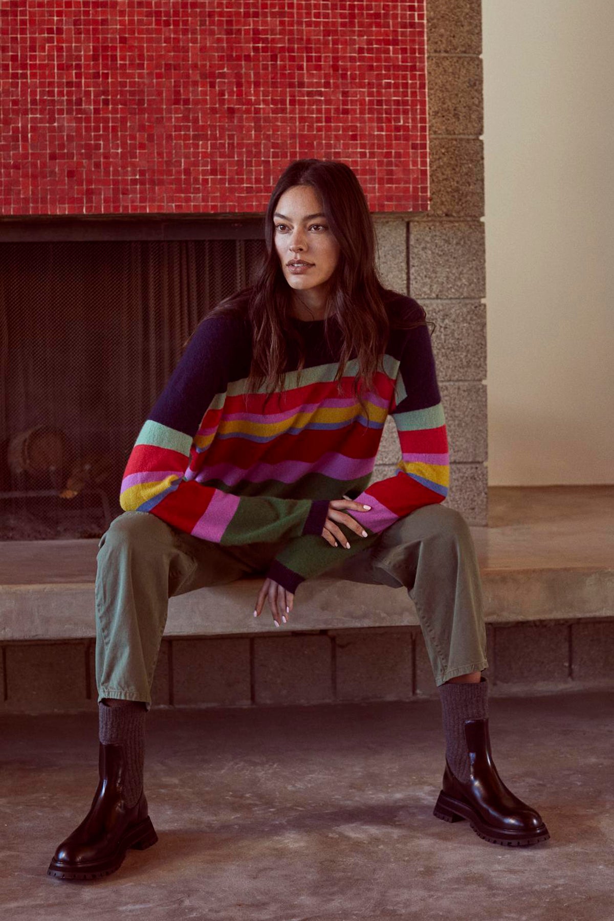 A woman in a KACEY CASHMERE STRIPED CREW NECK SWEATER by Velvet by Graham & Spencer sits on a fireplace.-26897828544705