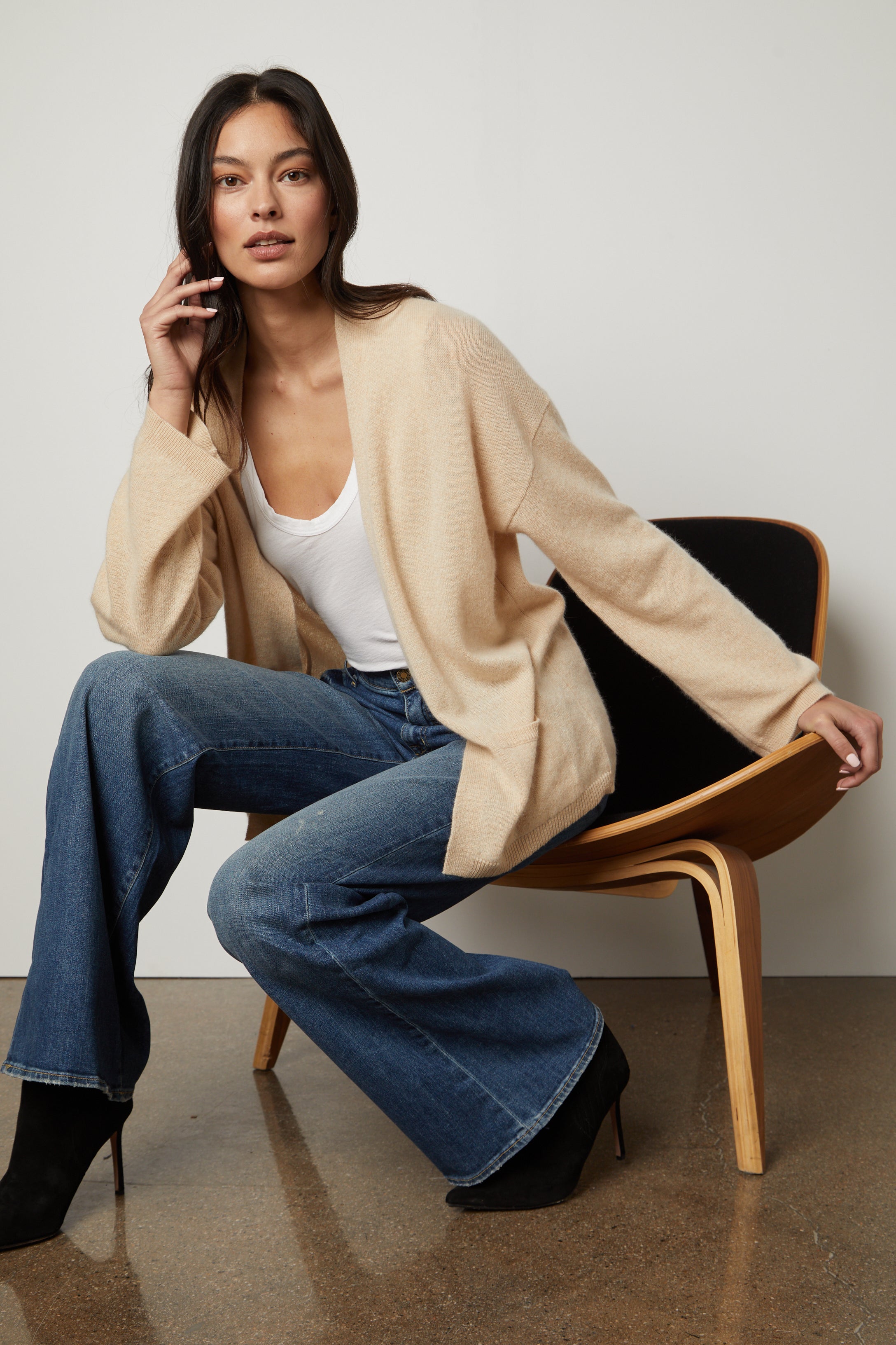   A woman in a LILA CASHMERE CARDIGAN by Velvet by Graham & Spencer sitting on a chair. 