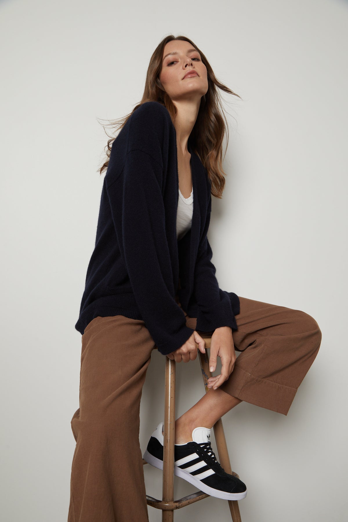   A woman is sitting on a stool wearing the Velvet by Graham & Spencer LILA CASHMERE CARDIGAN and pants. 