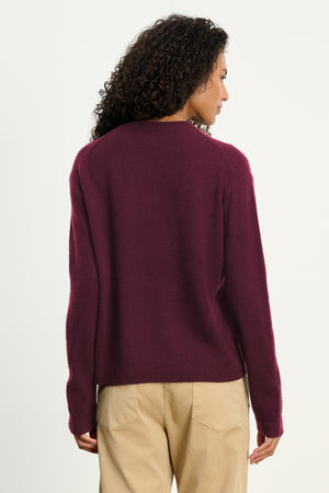 Person with curly hair shown from the back against a plain light background, wearing Velvet by Graham & Spencer's CRYSTAL CASHMERE SWEATER in burgundy with ribbed trims and beige pants.