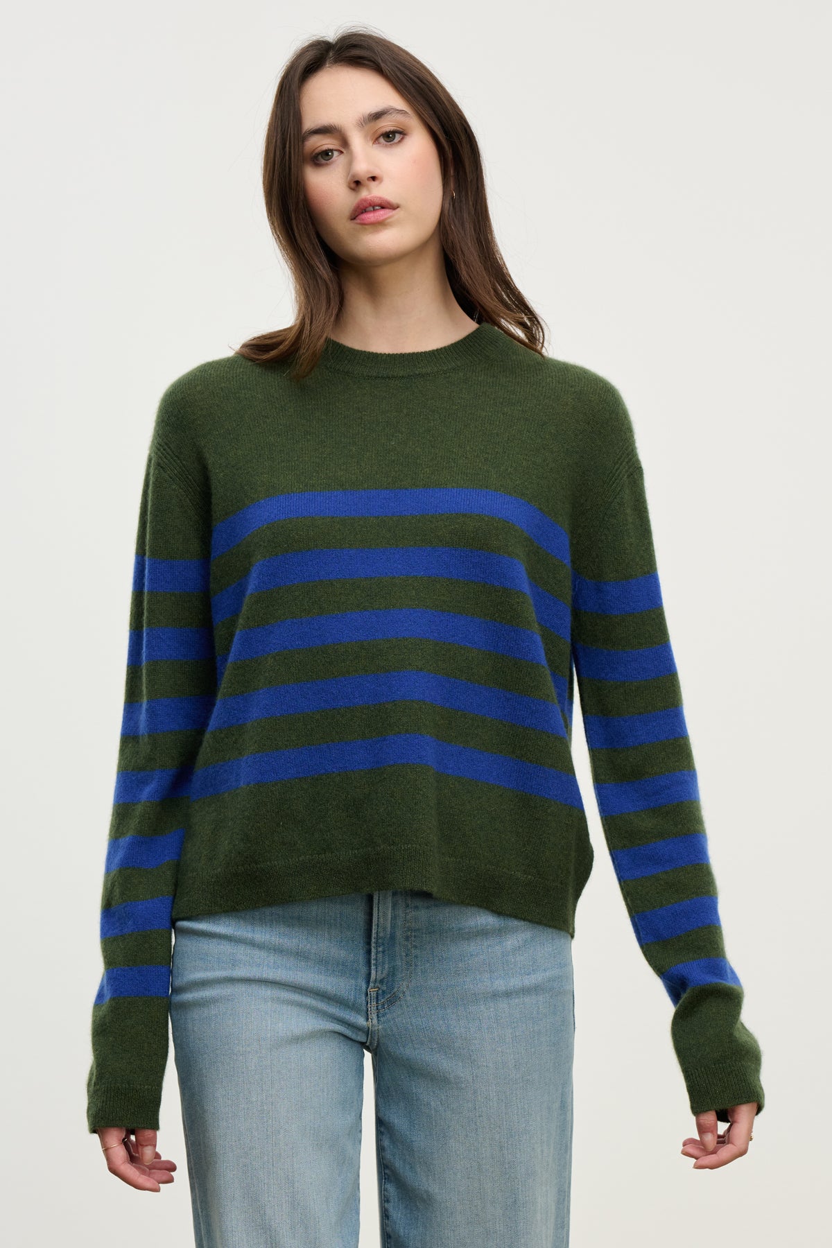 A person wears the DIANA CASHMERE SWEATER by Velvet by Graham & Spencer in green stripes, paired with light blue jeans, standing against a light-colored background.-39975057227969