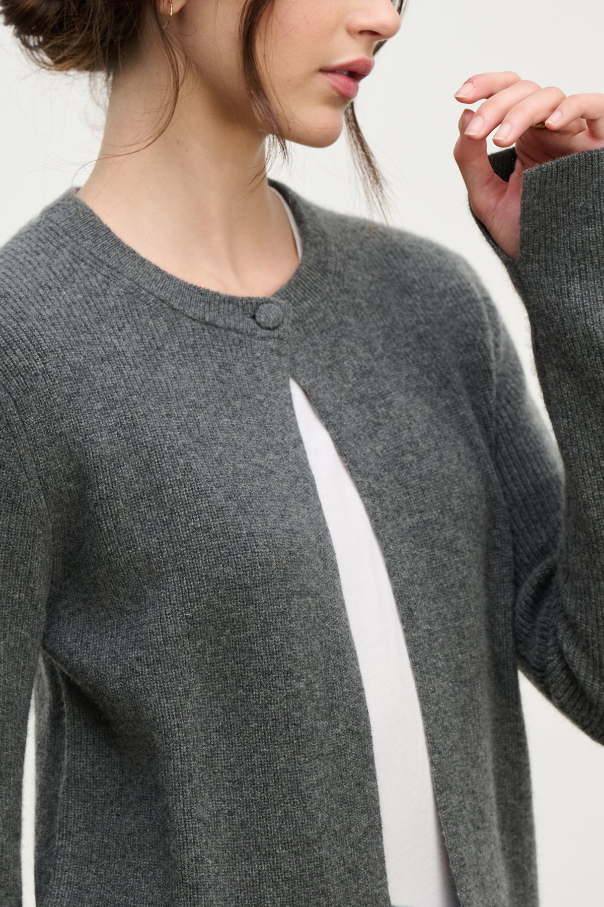 A woman wearing the TINA CASHMERE CARDIGAN by Velvet by Graham & Spencer—a grey, long-sleeve, buttoned cardigan with a subtle ribbed texture over a white top—makes it a perfect layering piece for any wardrobe.-39814940459201
