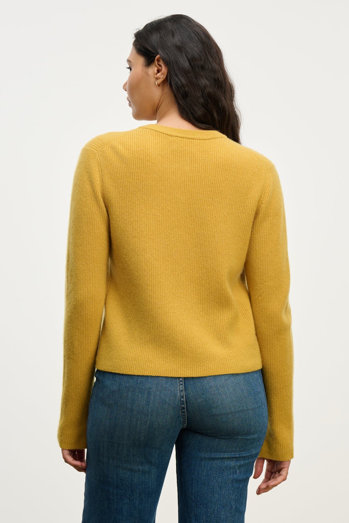 A woman is shown from the back wearing the Velvet by Graham & Spencer TINA CASHMERE CARDIGAN in mustard yellow with blue jeans against a plain background.-39814940197057