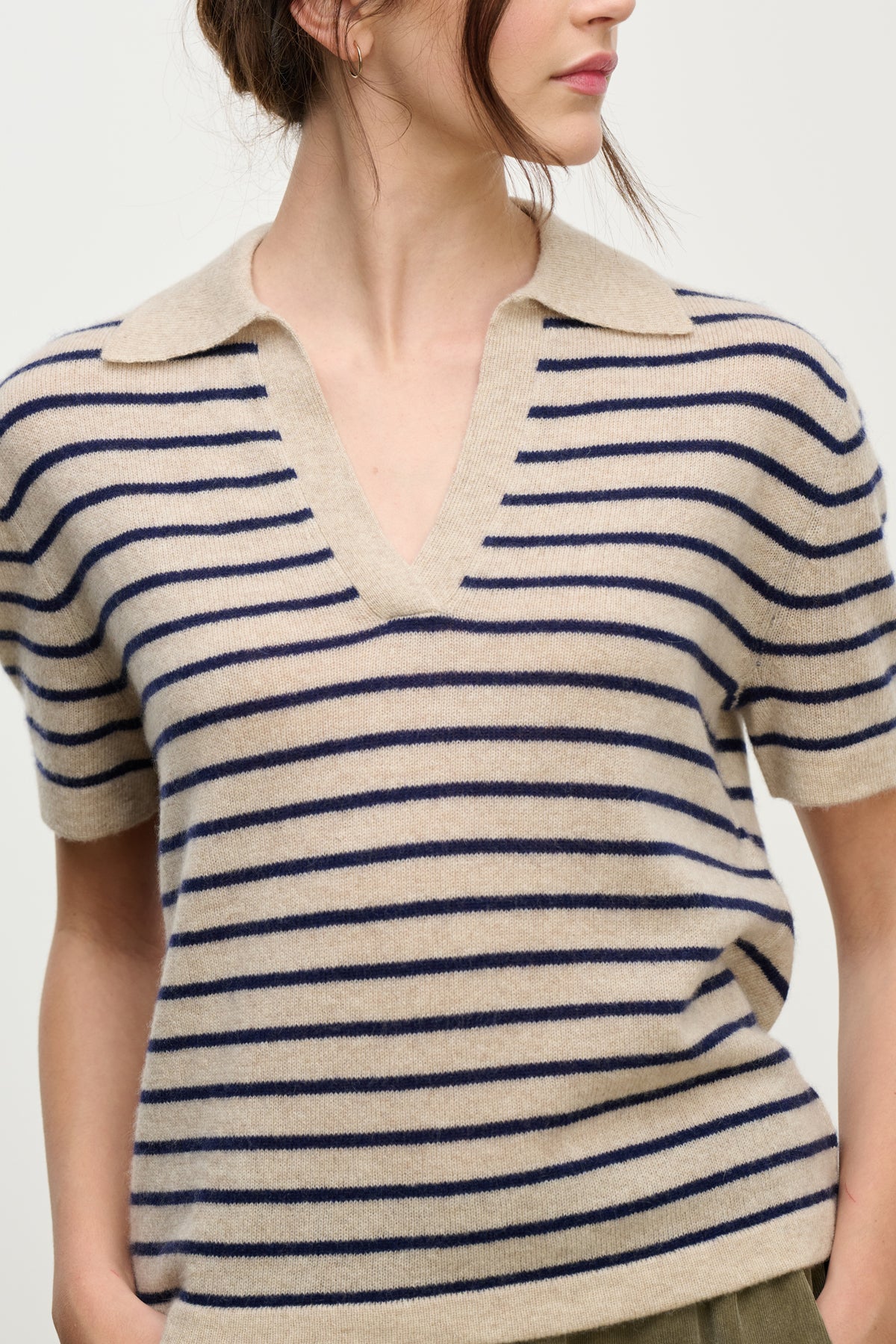   A woman wearing the YAEL CASHMERE SWEATER POLO by Velvet by Graham & Spencer, featuring beige cashmere with navy stripes and a wide V-neck collar, shown from shoulders to hips. 