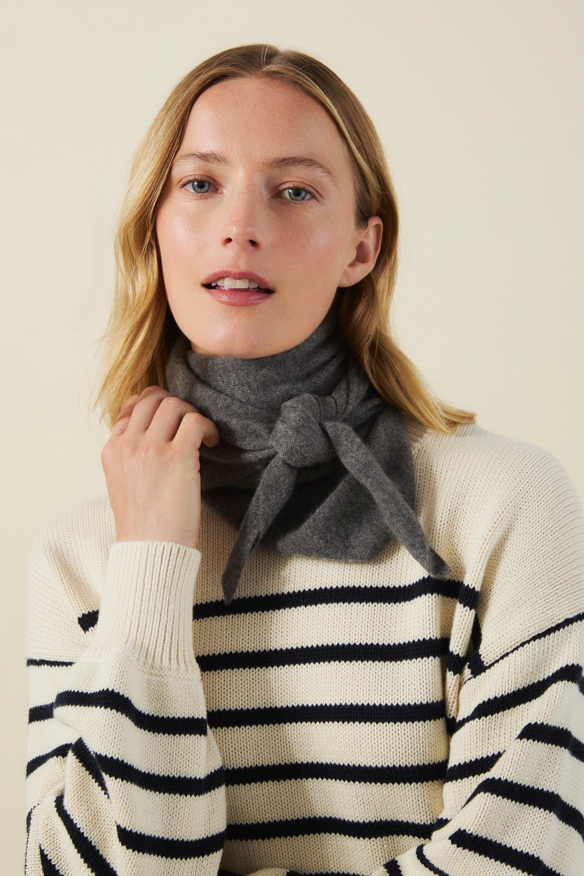 Woman wearing a dark gray CLEO CASHMERE TRIANGLE SCARF tied around her neck and a cream-colored sweater with horizontal navy stripes.
