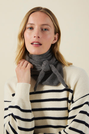 Woman wearing a dark gray CLEO CASHMERE TRIANGLE SCARF tied around her neck and a cream-colored sweater with horizontal navy stripes.