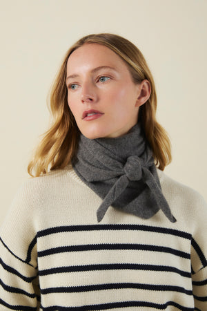 A person wearing a charcoal gray CLEO CASHMERE TRIANGLE SCARF tied around their neck over a cream and navy striped sweater.