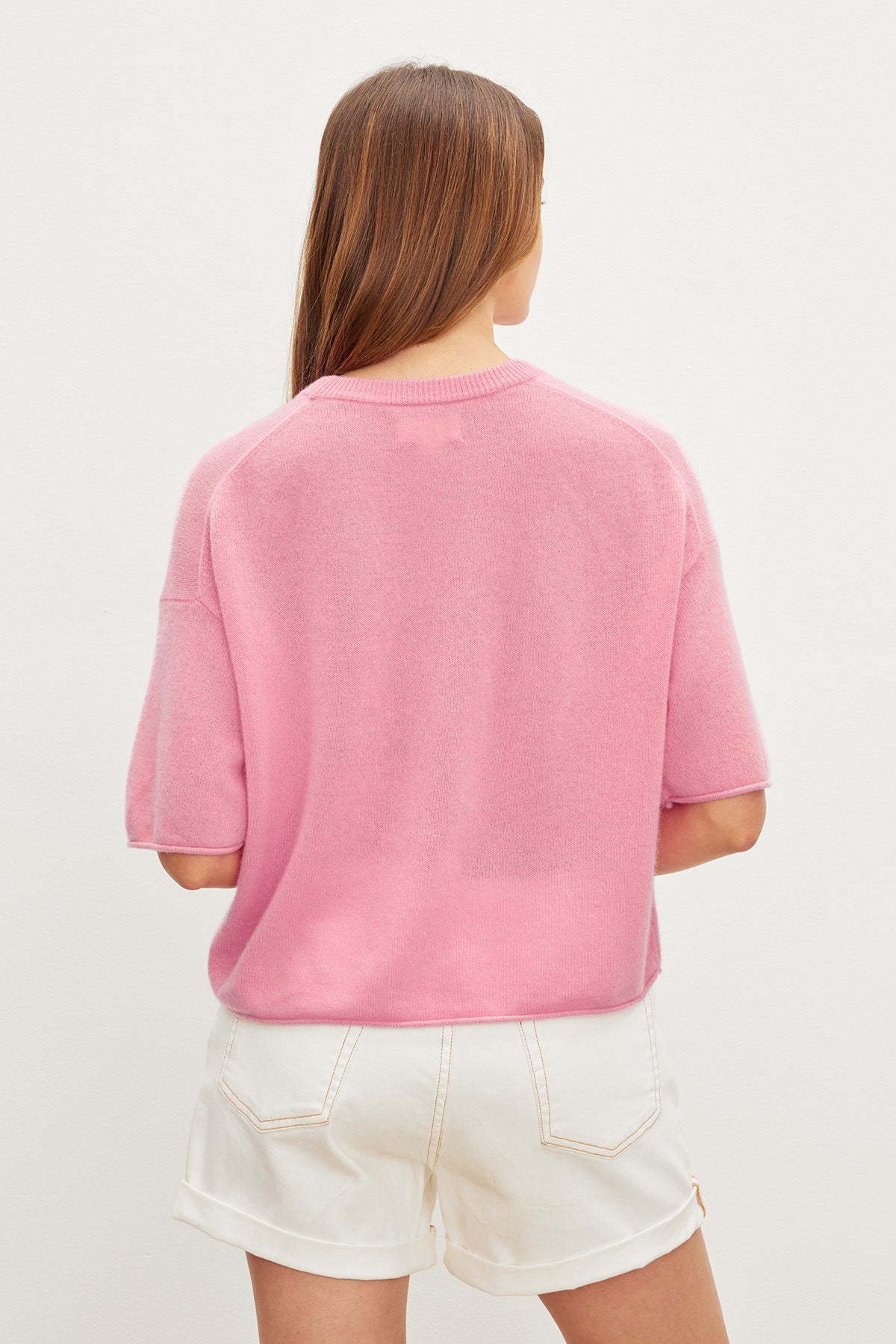   The back view of a woman wearing a Velvet by Graham & Spencer BLAKE CASHMERE CREW NECK SWEATER and white shorts with a versatile and cropped silhouette. 