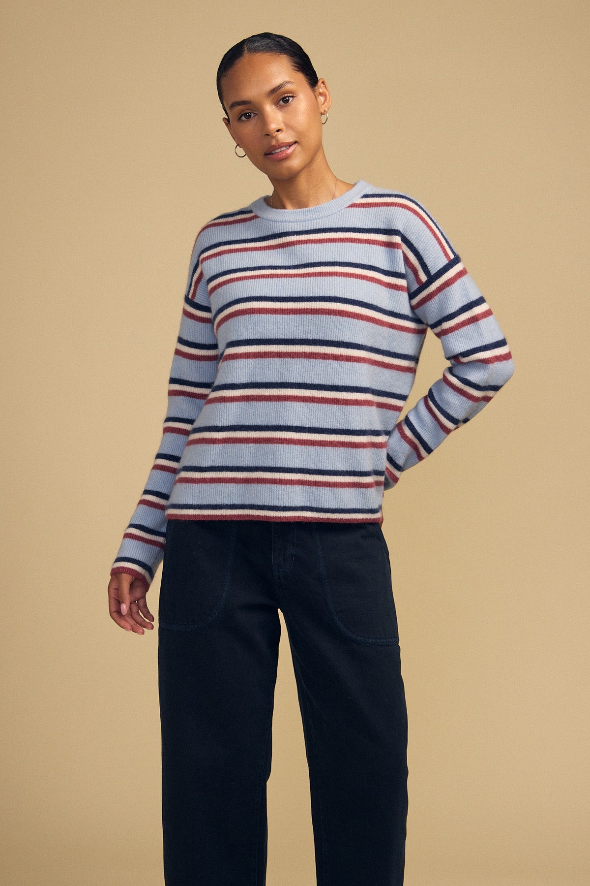 A person wearing a BETH SWEATER by Velvet by Graham & Spencer, a cozy knit crew neck with horizontal red, navy, and cream stripes, paired with dark pants.