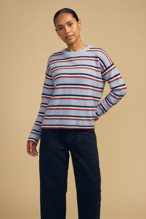 A person wearing a BETH SWEATER by Velvet by Graham & Spencer, a cozy knit crew neck with horizontal red, navy, and cream stripes, paired with dark pants.