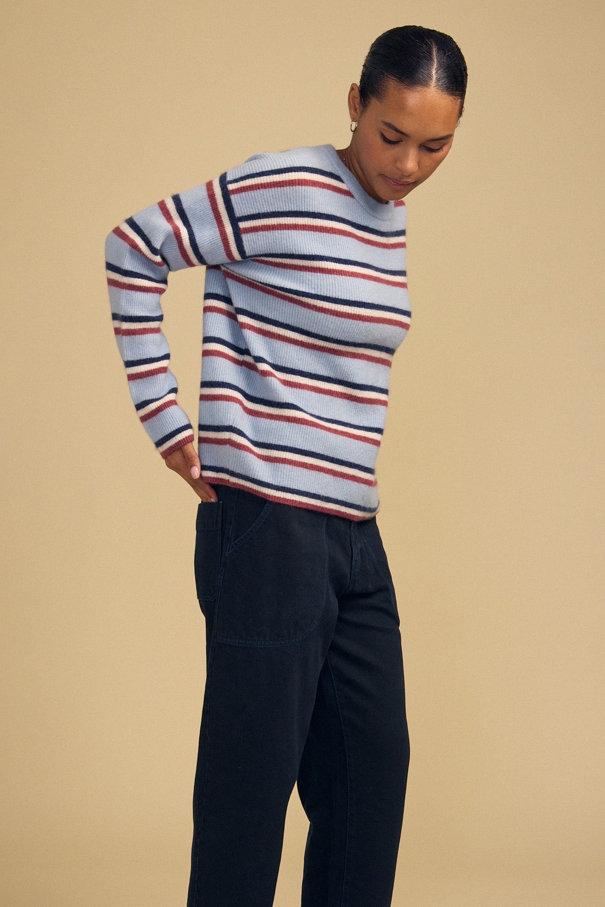Person wearing a cozy, light blue BETH SWEATER by Velvet by Graham & Spencer with horizontal red, navy, and white stripes, paired with dark trousers.