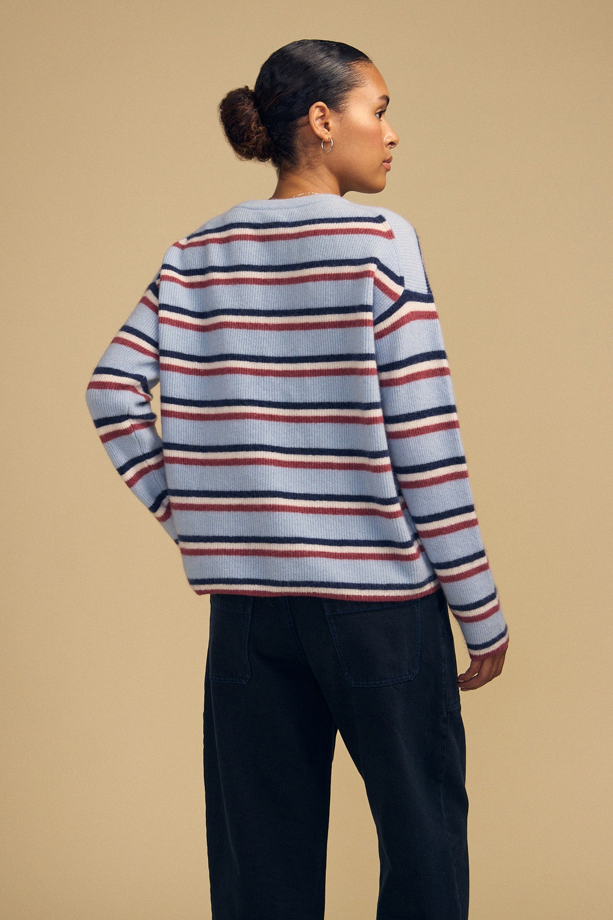 A person wearing the BETH SWEATER, a cozy knit crew neck with light blue, dark blue, and maroon horizontal stripes, paired with dark jeans.
