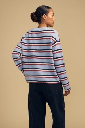 A person wearing the BETH SWEATER, a cozy knit crew neck with light blue, dark blue, and maroon horizontal stripes, paired with dark jeans.