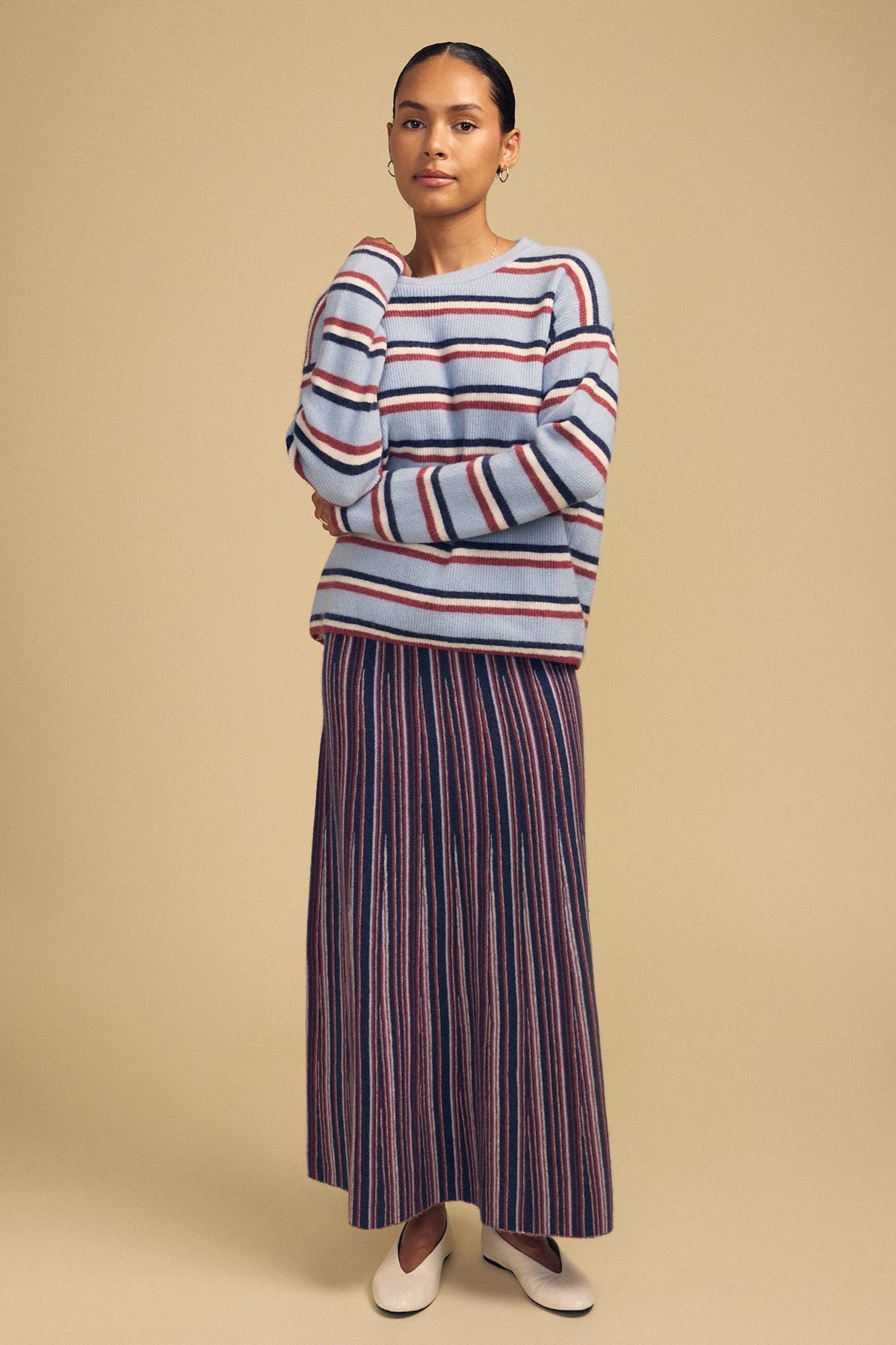 A person wearing a blue striped cashmere blend crewneck sweater, a Velvet by Graham & Spencer DESIREE FLARED SKIRT, and cream-colored flats.