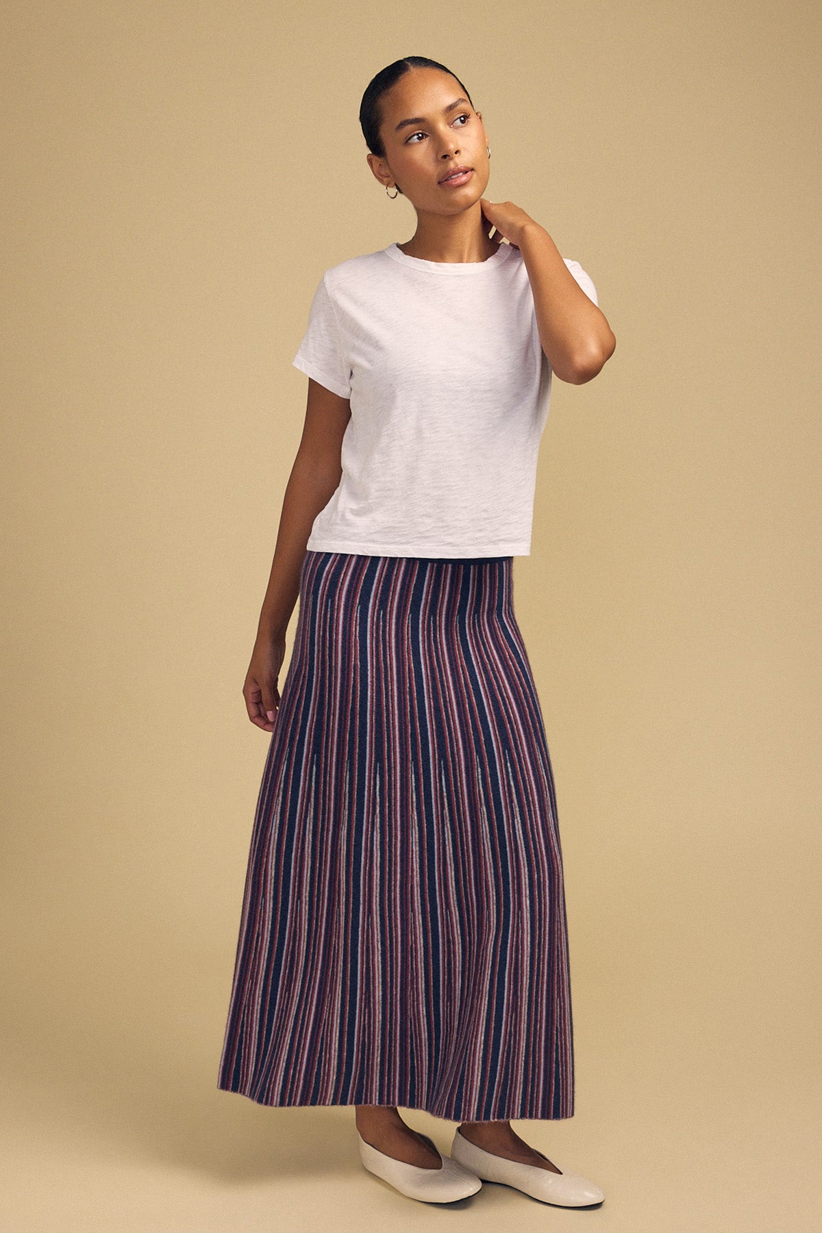A person wearing a white short-sleeved t-shirt, a multi-colored striped DESIREE FLARED SKIRT by Velvet by Graham & Spencer, and cream-colored flats.