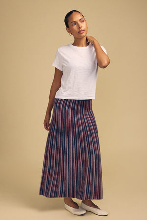A person wearing a white short-sleeved t-shirt, a multi-colored striped DESIREE FLARED SKIRT by Velvet by Graham & Spencer, and cream-colored flats.
