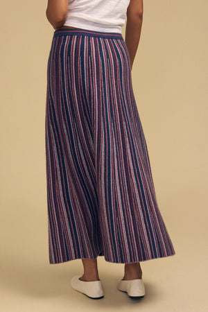 A person wears a white t-shirt and a DESIREE FLARED SKIRT, which is a calf-length skirt with a novelty texture and vertical red, white, and navy blue stripes.