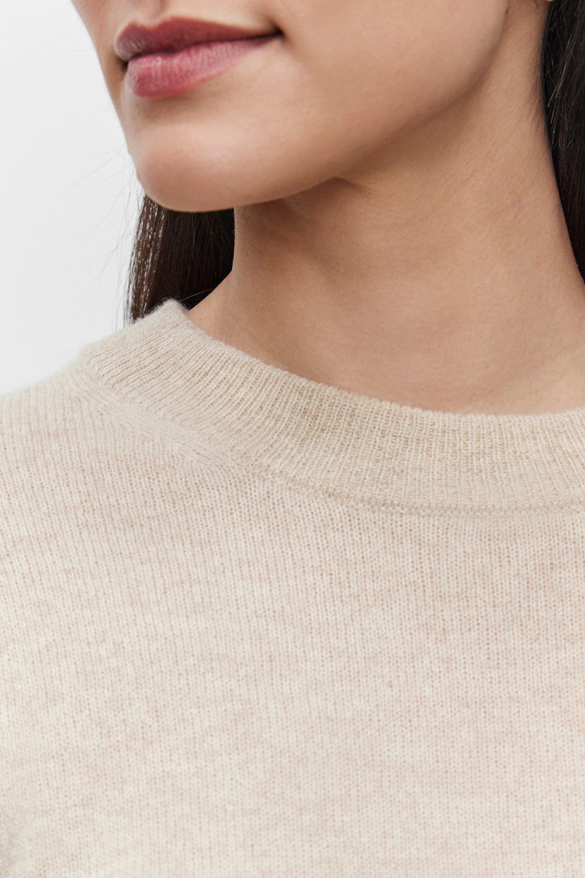 Close-up of a person's lower face and neck, showcasing the crew neckline and upper chest area of the beige BROOKLYN CASHMERE SWEATER by Velvet by Graham & Spencer, offering a contemporary look.