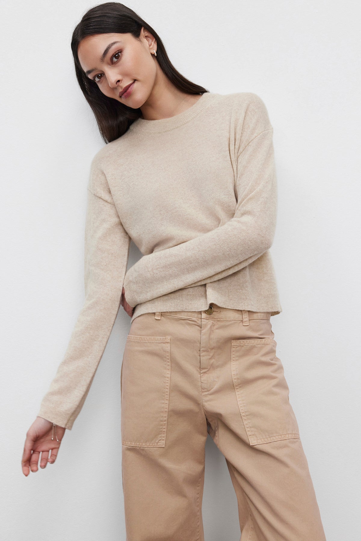   A person wearing the BROOKLYN CASHMERE SWEATER from Velvet by Graham & Spencer and light brown pants stands against a plain white background, showcasing a contemporary look. 