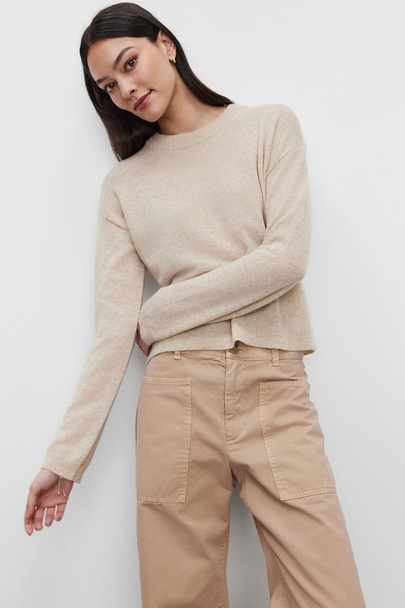 A person wearing the BROOKLYN CASHMERE SWEATER from Velvet by Graham & Spencer and light brown pants stands against a plain white background, showcasing a contemporary look.