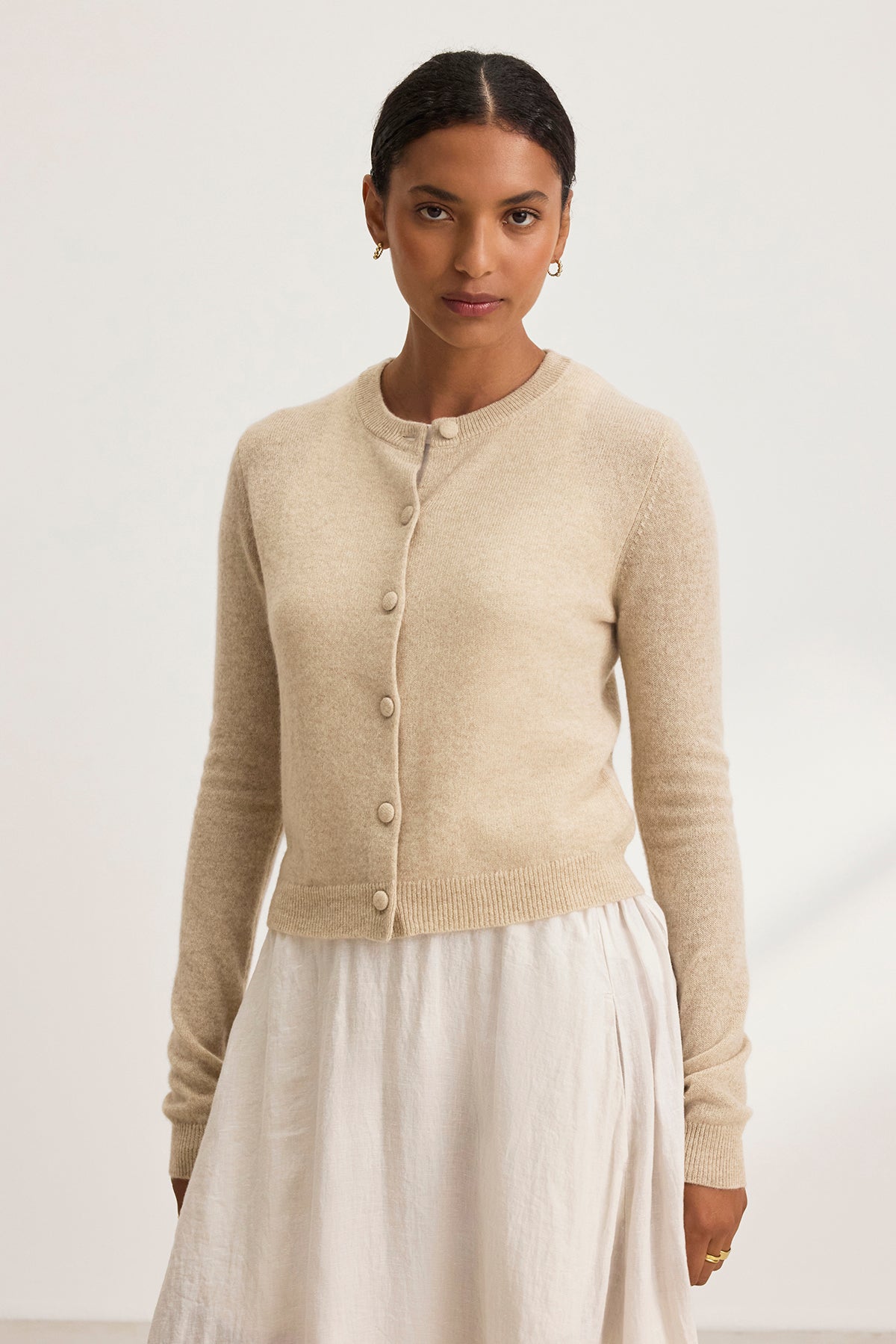 Someone wearing the CHRICHET CASHMERE CARDIGAN by Velvet by Graham & Spencer and a white skirt stands against a plain background.-38754141569217