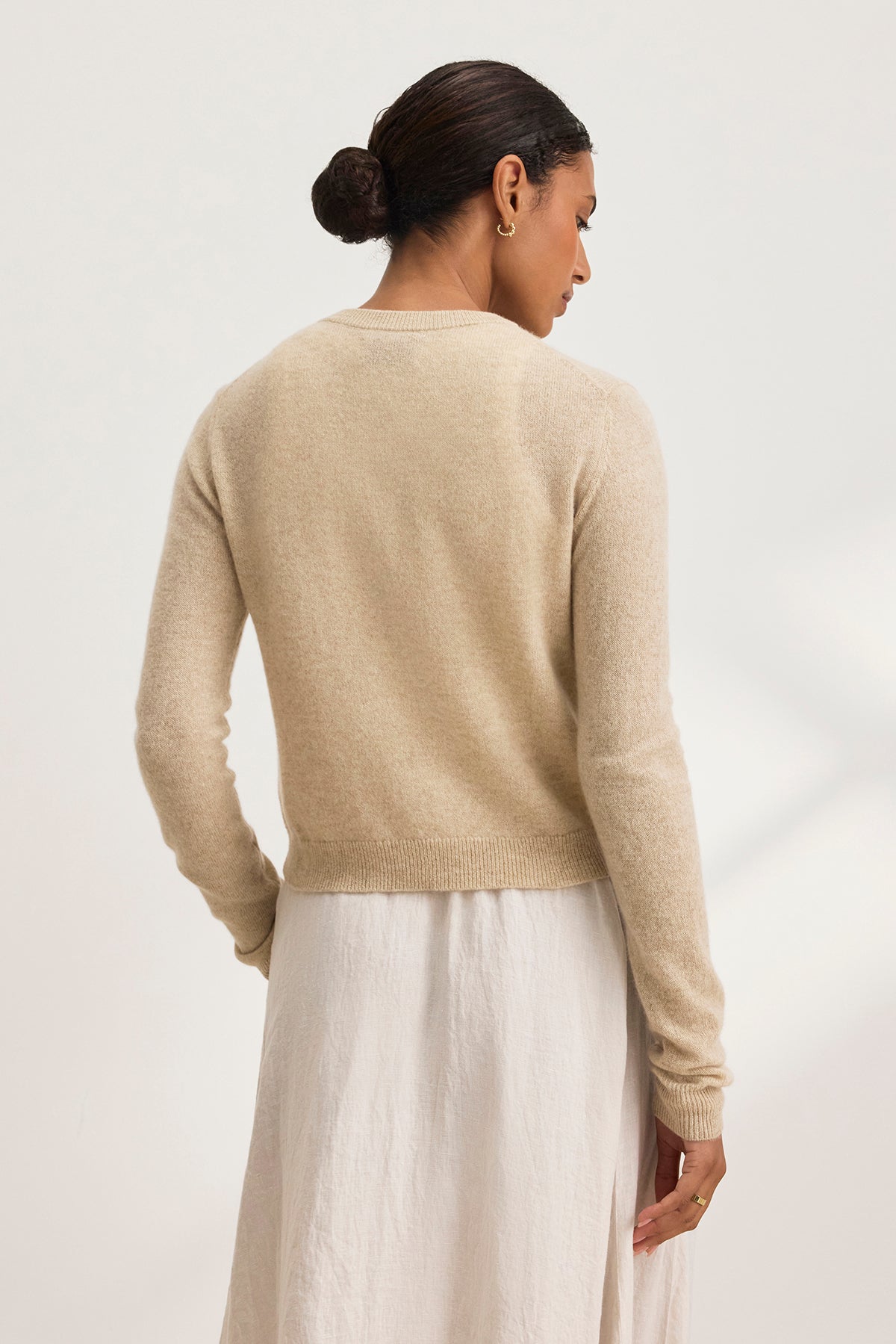 Person with dark hair in a bun, wearing the CHRICHET CASHMERE CARDIGAN by Velvet by Graham & Spencer and a white skirt, facing away.-38754141634753