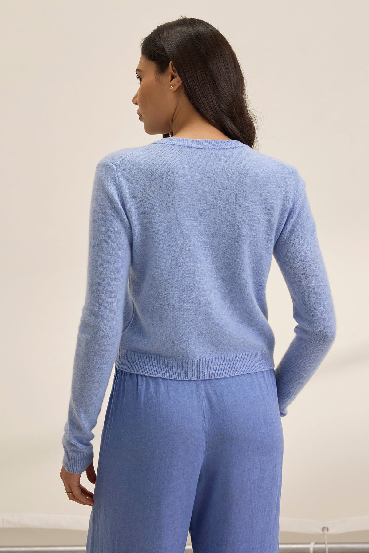 Individual with long hair wearing a Velvet by Graham & Spencer CHRICHET Cashmere Cardigan in light blue, facing away.-38754141798593