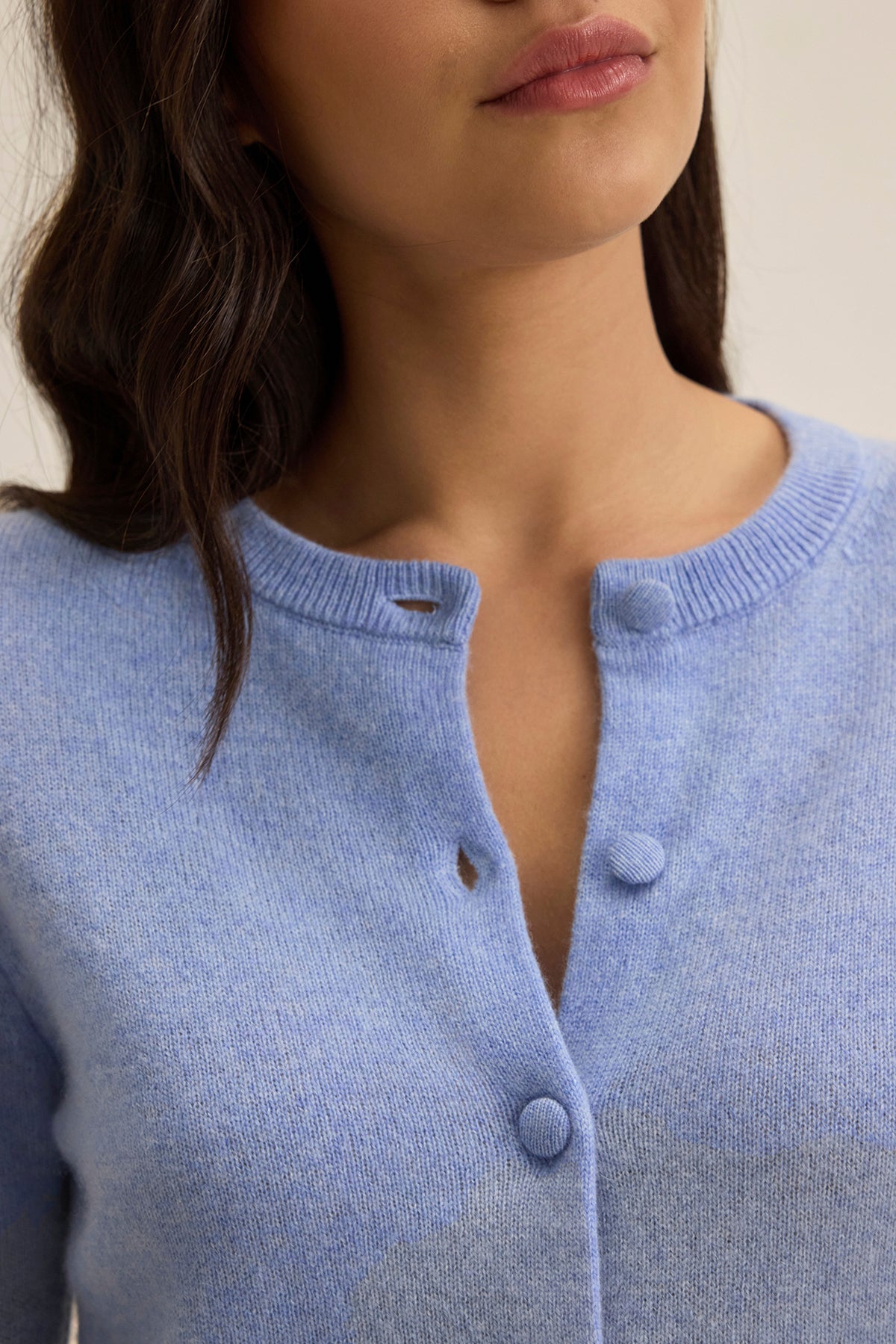 A woman wears a CHRICHET CASHMERE CARDIGAN by Velvet by Graham & Spencer in light blue with the top button undone. Her hair is dark and wavy.-38754141831361