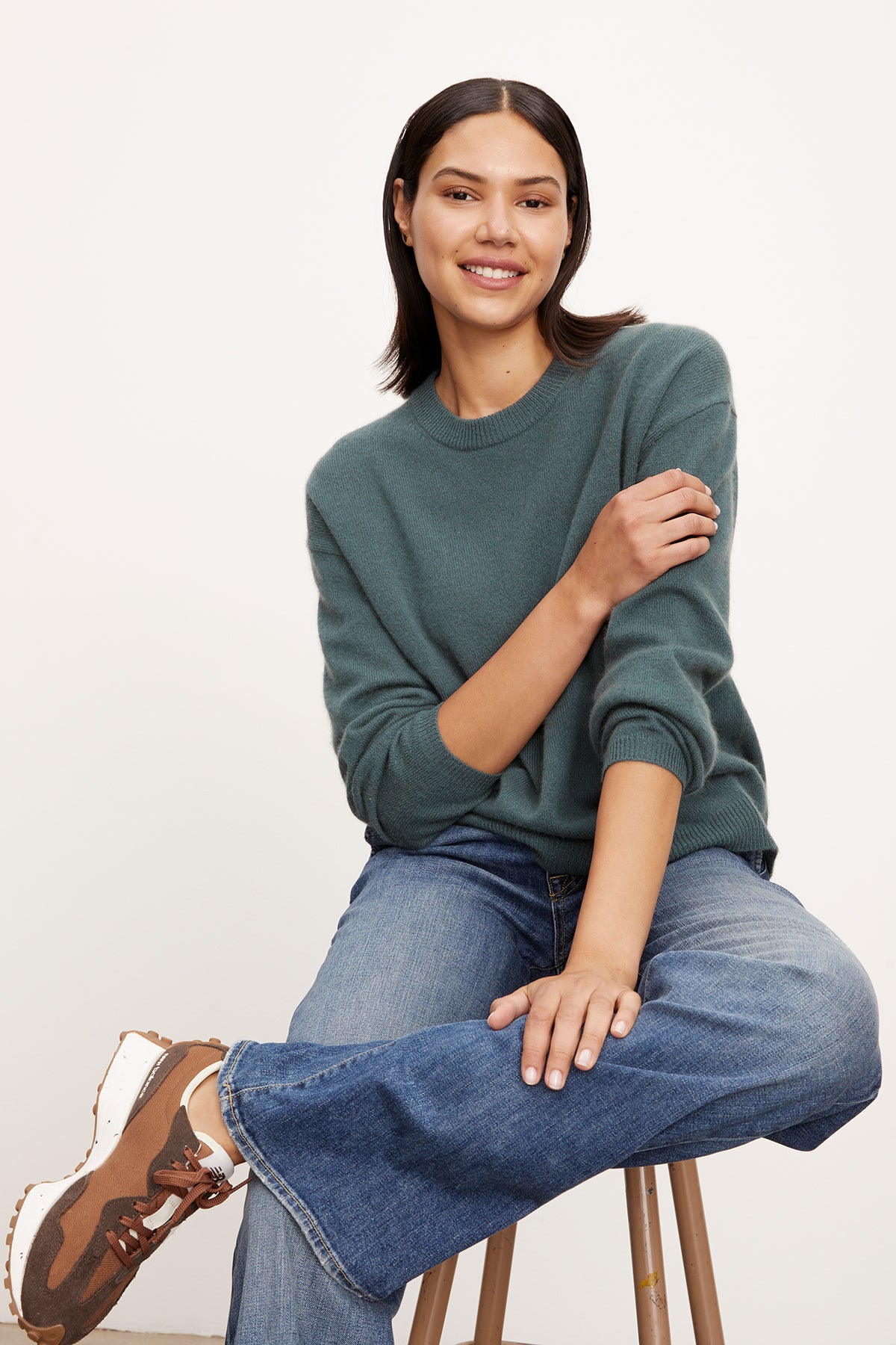   A woman is sitting on a stool wearing jeans and a Velvet by Graham & Spencer BRYNNE CASHMERE CREW NECK SWEATER with ribbed trims. 