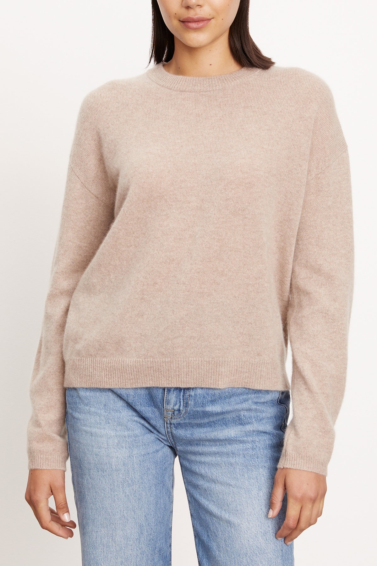 Model wears the BRYNNE CASHMERE SWEATER by Velvet by Graham & Spencer in light beige with ribbed trims and light blue jeans, standing against a plain white background.-40278713499841