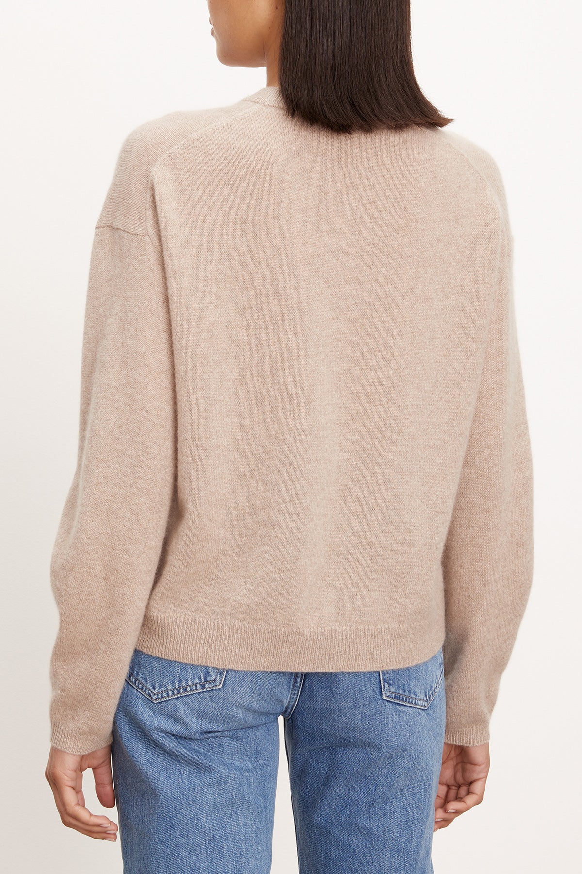 A person is seen from the back in a Velvet by Graham & Spencer BRYNNE CASHMERE SWEATER, beige with ribbed trims, paired with blue jeans against a plain light background.