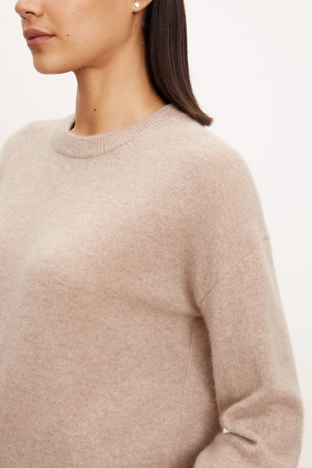 A person models the Velvet by Graham & Spencer BRYNNE CASHMERE SWEATER—a light beige, long-sleeve crewneck with ribbed trims—shown from shoulders to mid-torso against a plain background.-40278713630913