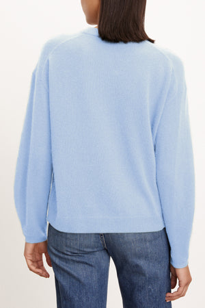 Model wears the BRYNNE CASHMERE SWEATER by Velvet by Graham & Spencer, a light blue crewneck with relaxed shoulders, paired with blue jeans. Shown from the back against a plain light background.
