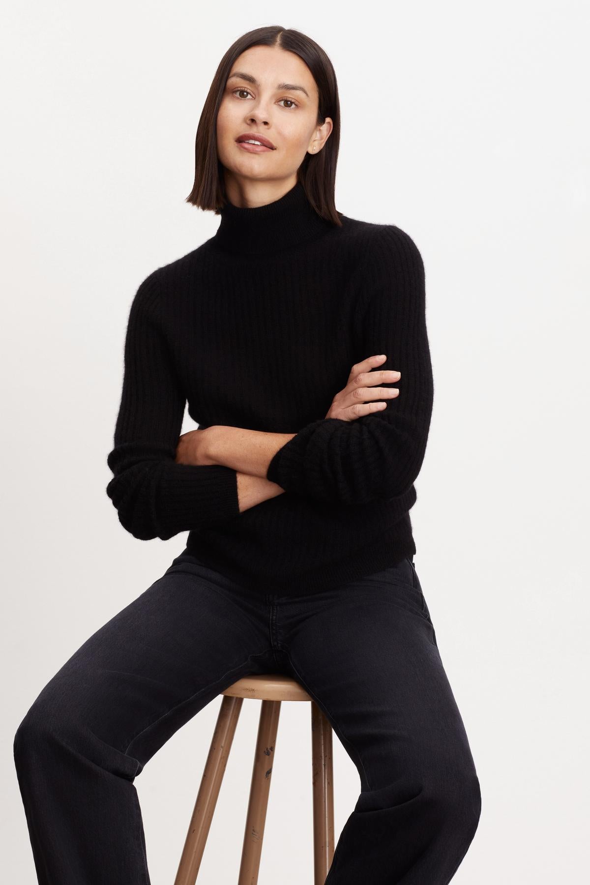A woman is sitting on a stool wearing a Velvet by Graham & Spencer Lori Cashmere Turtleneck Sweater.-35696186687681