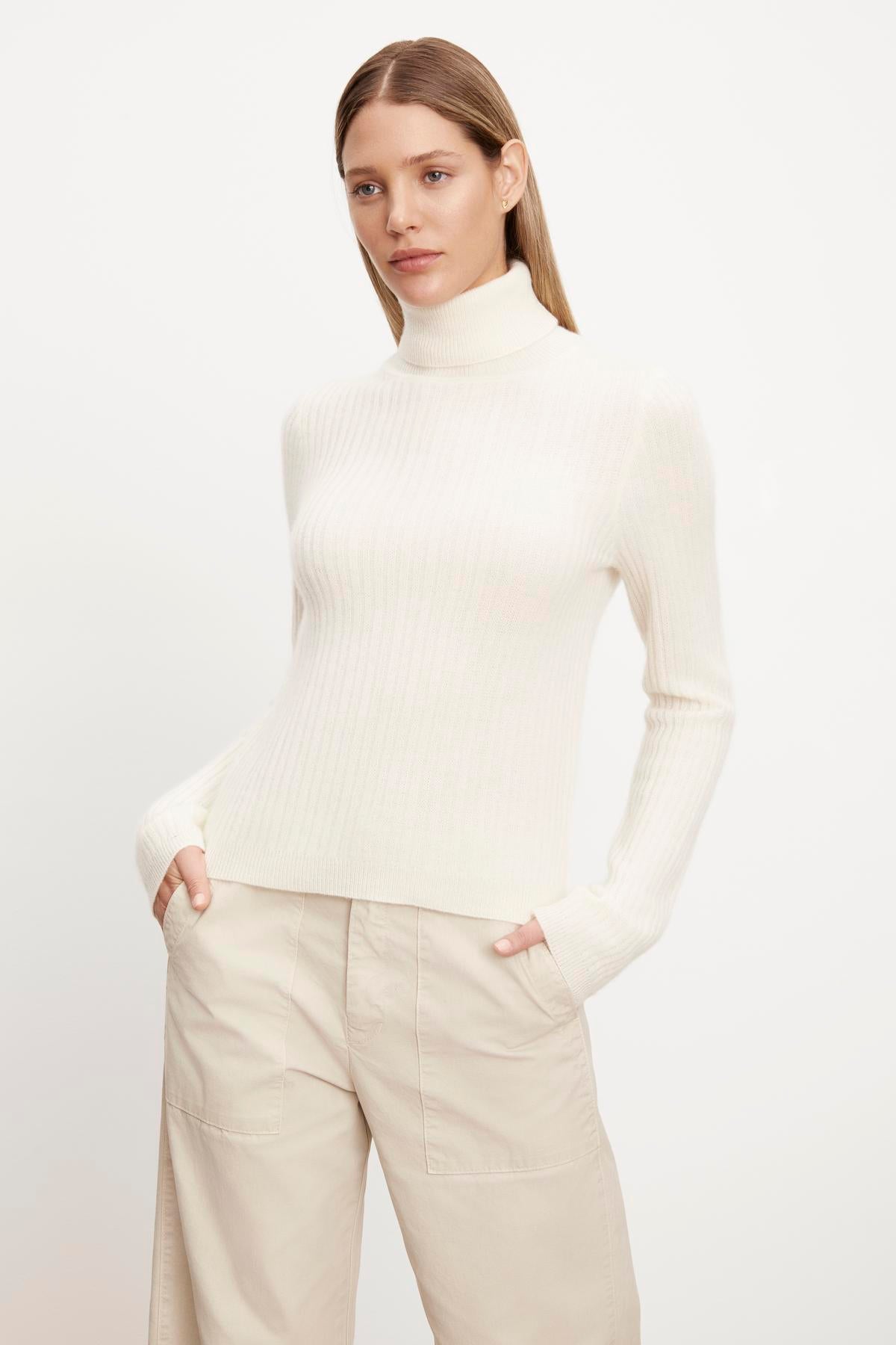   The model is wearing a LORI CASHMERE TURTLENECK SWEATER by Velvet by Graham & Spencer and beige trousers. 