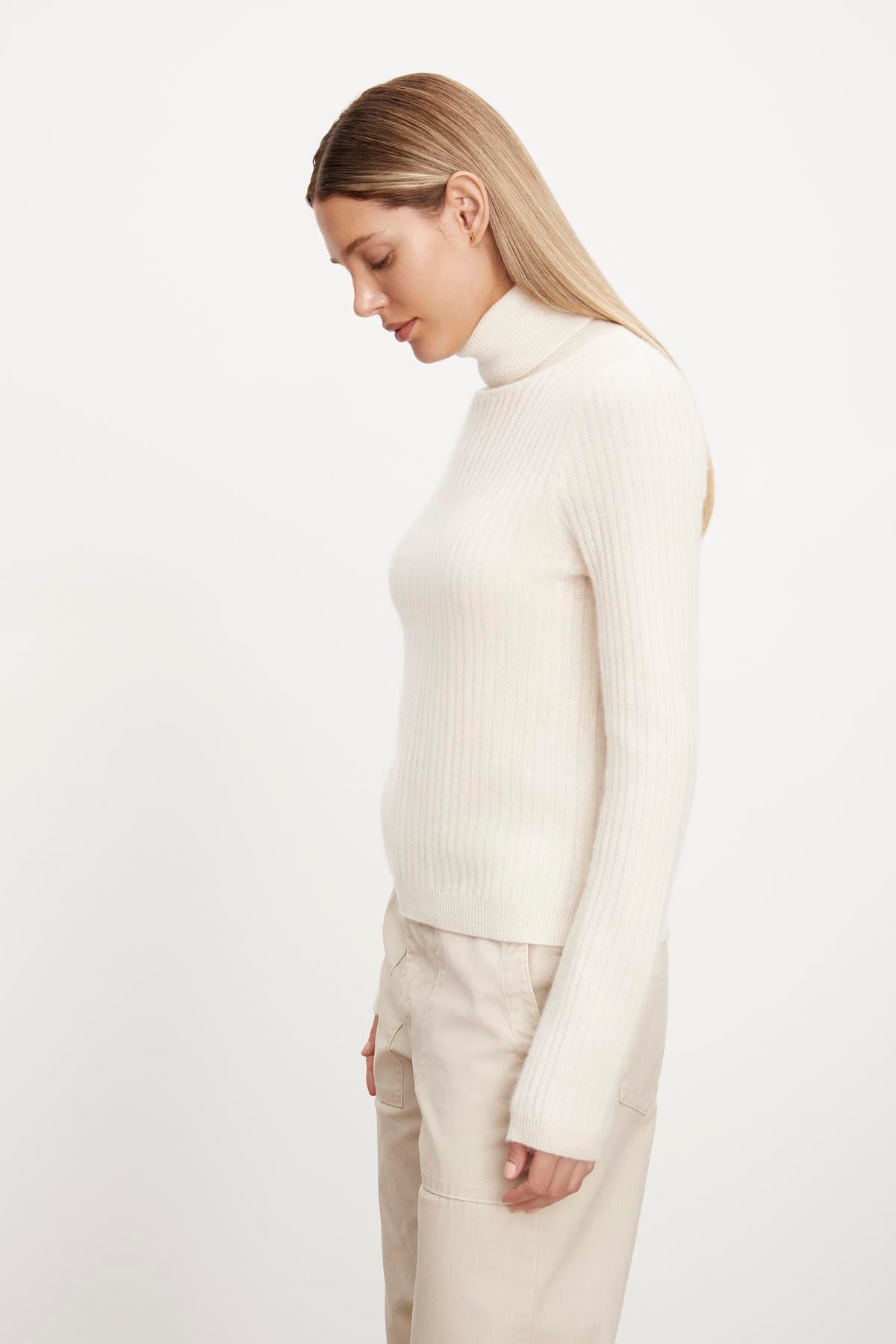   The model is wearing a white LORI CASHMERE TURTLENECK SWEATER by Velvet by Graham & Spencer and beige pants. 