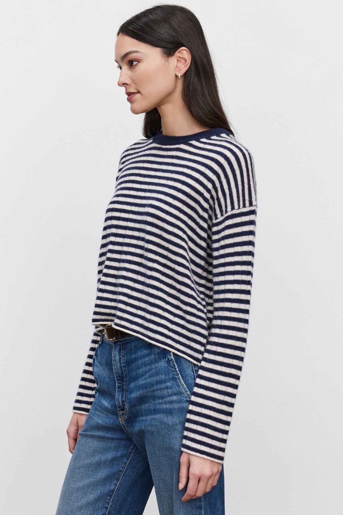   A woman with long dark hair models the MONICA CASHMERE SWEATER by Velvet by Graham & Spencer, paired with blue jeans. She stands against a plain white background, facing left, exuding luxury and comfort. 