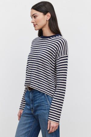 A woman with long dark hair models the MONICA CASHMERE SWEATER by Velvet by Graham & Spencer, paired with blue jeans. She stands against a plain white background, facing left, exuding luxury and comfort.