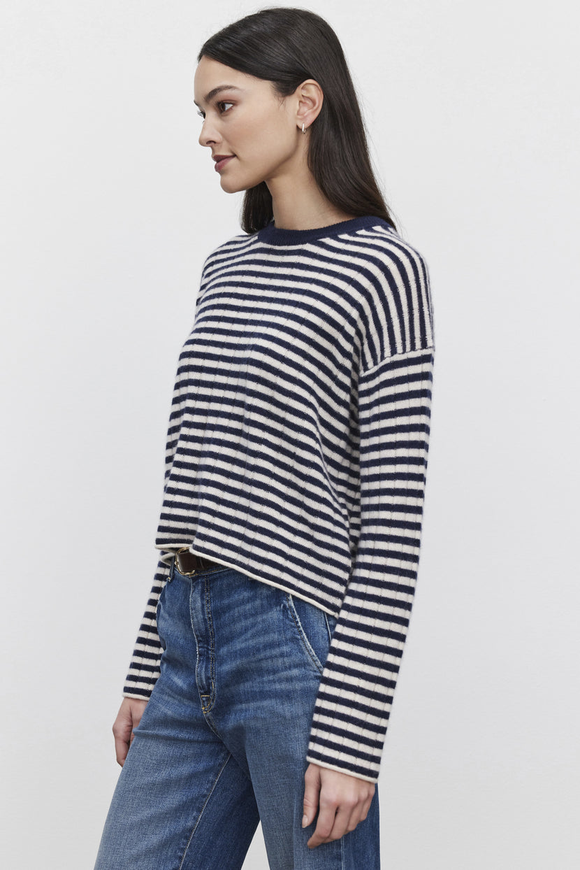 A woman with long dark hair models the MONICA CASHMERE SWEATER by Velvet by Graham & Spencer, paired with blue jeans. She stands against a plain white background, facing left, exuding luxury and comfort.