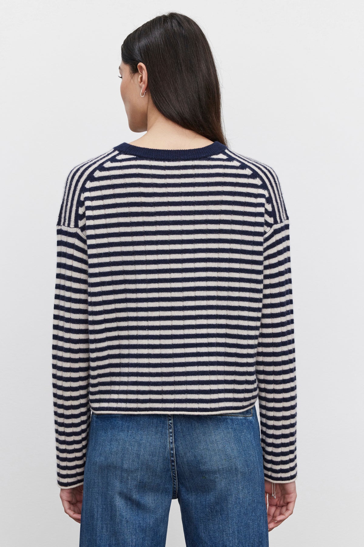   A person, seen from behind, dons the MONICA CASHMERE SWEATER by Velvet by Graham & Spencer. This navy and white striped piece with long sleeves complements their dark hair and denim jeans, embodying luxurious comfort. 